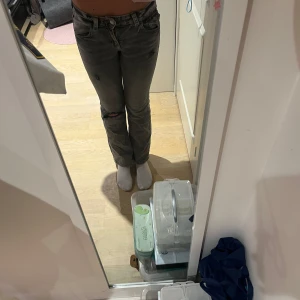 Grå bootcut jeans med slitningar - Säljer ett par grå jeans med bootcut-modell och snygga slitningar på benen. Jeansen har klassiska bakfickor med broderade detaljer och är i ett tvättat, lite blekt jeans tyg. Från Gina tricot. I stolek 158