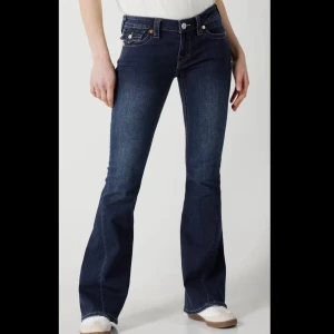 True Religion bootcut jeans mörkblå - Mörkblå jeans från True Religion med bootcut passform och snygga kontrastsömmar. Klassiska fickor bak med lock och dekorativa sömmar samt logopatch i midjan. Jeansen är tillverkade i stretchig denim för en bekväm känsla.
