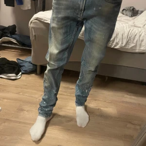 Blå skinny jeans från Zara, stl 38/30 - Säljer ett par blå skinny jeans från Zara med coolt sliten tvätt och vita färgstänk på benen. Jeansen har klassisk femficksdesign, normal midja och är tillverkade i bomull. Perfekta för dig som gillar en trendig och avslappnad look.