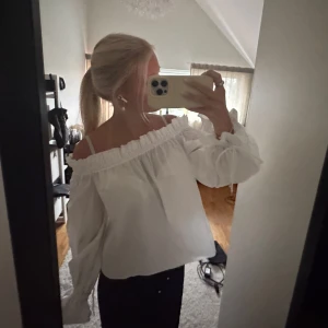 Vit offshoulder blus med knytärmar - Säljer en helt oanvänd vit offshoulder blus med volangkant upptill och långa ärmar med snygga knytband vid handlederna. 