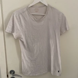 Vit t-shirt från Polo Ralph Lauren - Klassisk vit t-shirt från Polo Ralph Lauren med rund halsringning och korta ärmar. Tillverkad i mjuk bomull och har den ikoniska lilla broderade loggan i svart vid nederkanten. Enkel och stilren modell som passar till allt.