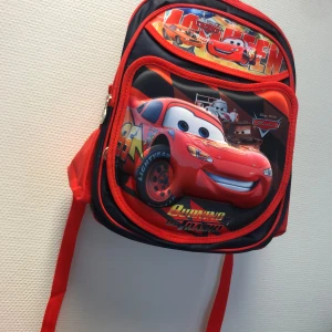 3D Cars ryggsäck - Cool ryggsäck med motiv från Cars , Väskan är svart och röd med flera fack, dragkedjor och meshficka på sidan. Perfekt för skolan eller utflykten, med justerbara axelband och färgglad design.