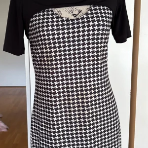 Svartvit rutig klänning Kim Kara - Snygg svartvit klänning från Kim Kara med klassiskt rutigt mönster. Modellen är figurnära med korta ärmar och rundad hals. Perfekt för dig som gillar grafiska prints och vill sticka ut med en cool look. Materialet känns mjukt och följsamt mot kroppen.