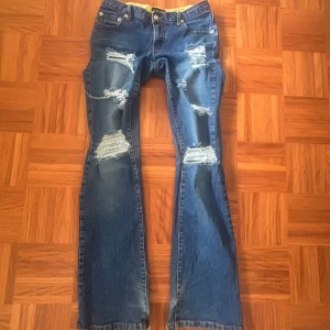 Blå bootcut jeans med slitningar Bik Bok - Säljer ett par blå bootcut jeans från Bik Bok i storlek M. Jeansen har flera slitningar och hål framtill för en edgy look, samt råa kanter vid bensluten. Klassisk femficksmodell med broderade detaljer på bakfickorna. Passar S. Öppen för prisdiskution