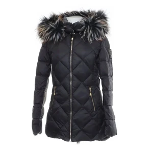 Svart pufferjacka från Chiara Forthi - Snygg svart pufferjacka från Chiara Forthi med lyxig fuskpäls runt huvan och guldfärgade dragkedjor. Jackan har quiltat mönster, två fickor med dragkedja och en patch på ärmen. Perfekt för kalla dagar när du vill vara både varm och stilren. Saknar en knapp vid den avtagbara huvan 