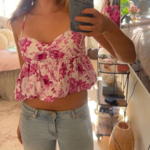 Rosa blommig linnetopp med volang - Supersöt linnetopp med rosa blommigt mönster på vit botten. Toppen har smala axelband, söt volang nertill och en lätt croppad passform. Perfekt för allt möjligt, middag eller fest! Säljer då den knappt används, köpt från Zara!💞pris kan diskuteras vid snabb affär💞