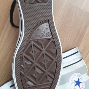 Converse All Star med stjärnor - Snygga Converse All Star sneakers i vitt och grått med coolt stjärnmönster och svarta snören. Klassisk hög modell med rund tå och vit gummisula. Perfekta för dig som vill sticka ut med en unik twist på klassikern.