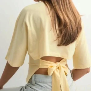 Nelly gul knyttopp  - Superfin ljusgul croppad topp med korta ärmar och snygg knytning i ryggen. Perfekt för varma dagar och ger en trendig look till jeans eller kjol. Kom privat för fler bilder! Använd fåtals gånger och säljer då den inte kommer till användning