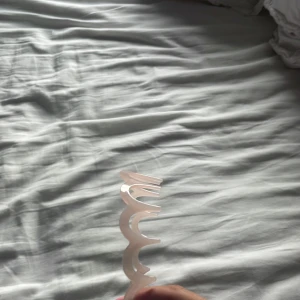 Vågigt ljusrosa diadem i plast - Säljer ett unikt diadem i ljusrosa plast med vågig design. Diademet har en cool, modern look och är perfekt för att hålla håret på plats med stil. Passar dig som vill sticka ut med accessoarer som känns trendiga och lekfulla.