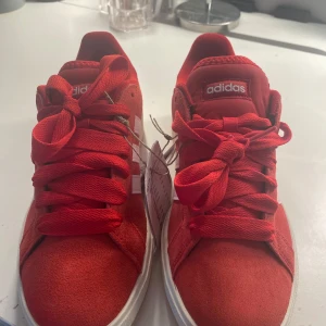 Röda Adidas sneakers med vita ränder - Snygga röda Adidas sneakers med klassiska vita ränder på sidorna och vit sula. Skorna har en rund tå, breda röda skosnören och ovandel i mocka. Perfekta för dig som vill sticka ut med färg och sportig stil. Aldrig använt, prislappen kvar!!