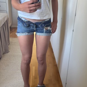 Lågmidjade jeansshorts med slitningar från 2000s - Snygga lågmidjade jeansshorts från vintage Cheap Monday i klassisk blå denim. Shortsen har slitningqr som gör att dom ser extra coola ut. Shortsen är från 2000s cheap monday och är köpta runt 2000s. 