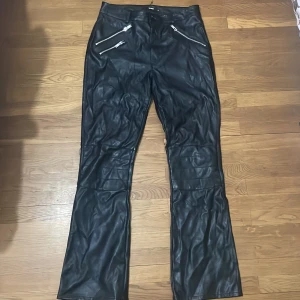 Svarta skinnbyxor med bootcut - Säljer ett par svarta skinnbyxor med bootcut och markerade sömmar över benen. Byxorna har en snygg glansig finish. Passar till många olika stilar och är riktigt trendiga just nu.
