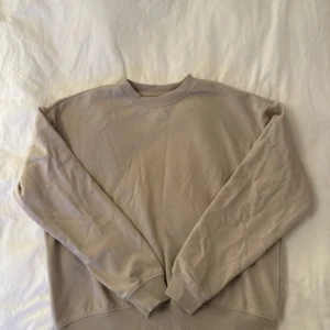 Beige sweatshirt med rund hals - En enkel och stilren beige sweatshirt med rund hals och långa ärmar. Tröjan har en loose passform och är gjord i mjuk bomull, perfekt för chill dagar. Ribbstickade muddar vid ärmslut och nederkant ger en snygg touch. Passar dig som gillar neutrala färger och comfy vibes.