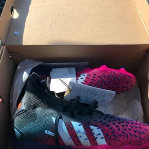 Adidas Predator rosa/svarta fotbollsskor -  Storlek: 40 2/3. Säljer ett par Adidas Predator fotbollsskor i en riktigt fet färgkombo med svart och rosa, samt vita ränder på sidan. Skorna har en strumpliknande ovandel. Tyvärr har jag inte kvar snörena  men dem sitter riktigt bra utan snören, dessutom riskerar man inte att snörningen går upp vid användning.