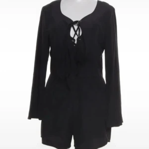 Svart romper - Snygg svart kort romper med långa ärmar och snörning framtill vid halsen. Den har en enkel och stilren design med lätt v-ringad hals och mjukt fallande tyg. Perfekt för dig som gillar minimalistisk stil med en twist.Romper / byxdress / shortsdress / playsuit från Neon Rose. Använd 1-2 gånger, mkt bra skick.  Storlek 10, motsvarar 38