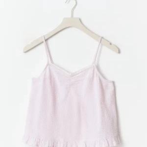 Ljusrosa linnetopp från Gina Tricot - Supersöt ljusrosa linnetopp från Gina Tricot med smala axelband och volangkant nedtill. Toppen har en lätt textur i tyget och v-ringad halsringning. Perfekt för varma dagar eller som ett gulligt lager under en kofta.