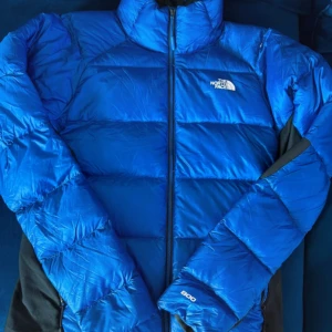 Blå dunjacka från The North Face M - Säljer en blå dunjacka från The North Face i storlek M. Jackan har en klassisk pufferstil med hög krage, svart foder och dragkedja framtill. Perfekt för kalla dagar och riktigt snygg färg som sticker ut. 800 fill power för extra värme.