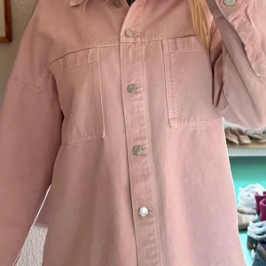 Ljusrosa jakke - zara - Säljer en ljusrosa jakke med silverfärgade knappar och två stora bröstfickor. Skjortan har en loose passform och långa ärmar