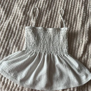 Vit smockad linnetopp Gina Tricot - Supersöt vit linnetopp från Gina Tricot i storlek XXS. Toppen har smala axelband, smockad överdel och en lätt utställd volang nertill. Materialet är mjukt och har en vågig struktur som ger en chill och somrig vibe.