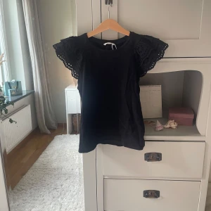 Svart blus med broderade volangärmar - Supersöt svart blus från Reserved med broderade volangärmar som ger en extra touch. Toppen har rund halsringning och är i mjukt material, perfekt för dig som gillar en stilren men ändå unik look.