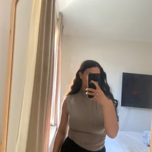 Ärmlös mock neck topp i tre färger - Säljer tre stilrena ärmlösa mock neck-toppar i svart, beige och brun. De har en tight passform och är tillverkade i mjukt, stretchigt material som sitter snyggt mot kroppen. Perfekt till jeans eller kjol för en clean look.