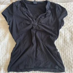 Y2k tröja  - Svart blus i bomull med korta ärmar och djup v-ringning. Kragen och ringningen är dekorerade med fina spetsdetaljer som ger en romantisk vibe. Ger lite Elena Gilbert vibe, och sitter jättefint. 