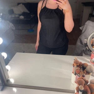 Svart linnetopp med smala axelband Gina Tricot - Säljer en svart linnetopp från Gina Tricot med smala dubbla axelband som korsas i ryggen. Toppen har lätt plisserad struktur och är ärmlös med en lös passform. Perfekt att styla med jeans eller kjol för en trendig look.