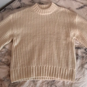Vit stickad tröja från 157 - Säljer en mysig vit stickad tröja från 157 med ribbad struktur och hög krage. Tröjan har långärmade ärmar och breda muddar vid ärmslut och nederkant. Perfekt för att hålla sig varm under kyliga dagar. Passar dig som gillar enkel och clean stil. Passar även dig som har storlek S. Tröjan är aldrig använd!