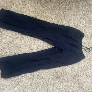 Mörkblå linnebyxor från Gina Tricot - Snygga mörkblå linnebyxor från Gina Tricot med avslappnad passform och resår i midjan med snörning. Byxorna har raka, vida ben och är perfekta för en chill och stilren look. Materialet är svalt linne och de har praktiska sidfickor.