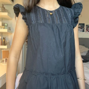 Svart blus med spets från H&M - Supersöt svart blus från H&M med volangärmar och detaljerad spets upptill. Rund halsringning och luftig passform. Blusen går ut lite vid midjan/höfterna. 