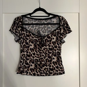 Leopardmönstrad topp från Romwe - Superfin leopardmönstrad topp från Romwe i storlek S. Toppen har korta ärmar, v-ringning med söt svart rosett och dekorativ spetskant. Materialet är lätt och stretchigt, perfekt för att sticka ut. Färgerna går i beige, brunt och svart.