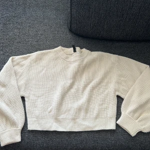 Beige croppad stickad tröja - Säljer en beige croppad stickad tröja med långärmade och breda muddar. Tröjan har en högre rundad hals och är perfekt för dig som gillar en chill och stilren look. 