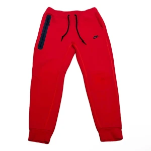 Nike tech - Riktigt snygga röda mjukisbyxor från Nike med svart logga på benet. Byxorna har svarta snören i midjan, ribbade muddar och en cool dragkedjeficka på sidan. Perfekta för chill eller träning, tillverkade i mjukt material för maxad komfort. Liten fläck på sista bild kan nog bli borttvättad.