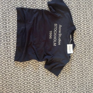 Svart Acne Studios t-shirt Stockholm - Svart t-shirt från Acne Studios med tryck 'Stockholm 1996' i vitt på framsidan. Modellen är loose fi. Materialet är mjuk bomull och köpt vintage men kvar lappen