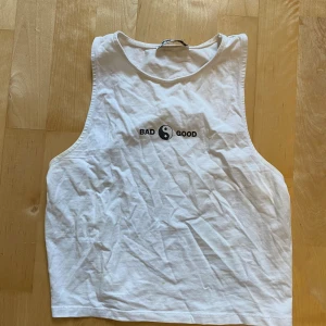 Vit linnetopp från FB Sister - Säljer en vit linnetopp från FB Sister i storlek M. Toppen har ett tryck med yin-yang-symbol och texten 'BAD GOOD' på bröstet. Modellen är ärmlös och har en rund halsringning. Perfekt för dig som gillar minimalistisk stil med en cool detalj.