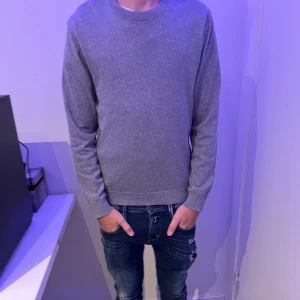 Grå stickad tröja med rund hals - En enkel och stilren grå stickad tröja med rund hals och långa ärmar. Passformen är normal och materialet känns mjukt mot huden. Perfekt att matcha med jeans eller andra favoritplagg. Snyggt basic-plagg för dig som gillar minimalistisk stil.