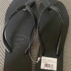 Svarta flip-flops från Havaianas - Svarta flip-flops från Havaianas med klassisk design och mönstrad sula. Remmarna är i svart syntetmaterial med Havaianas-logga. Perfekta för stranden eller varma dagar.