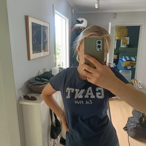 Mörkblå GANT t-shirt med tryck - Snygg mörkblå t-shirt från GANT i mjuk bomull. Klassisk rund hals och vit tryckt logga med 'GANT Est. 1949' på bröstet. Passformen är normal och ärmarna är korta. Perfekt för dig som gillar stilrena och sportiga plagg med preppy-vibe.