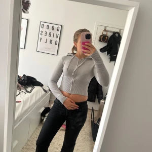 Grå croppad hoodie med dragkedja - Säljer en ljusgrå croppad hoodie med dragkedja och snörning i huvan. Tröjan är stickad och har långa ärmar samt ribbad nederkant och muddar. Perfekt för dig som gillar en chill och trendig look.