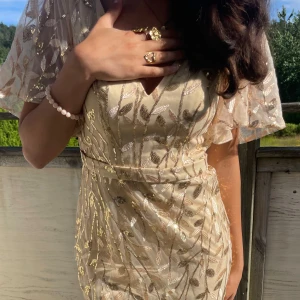 Champagnefärgad långklänning med skimmer - Säljer en magisk champagnefärgad långklänning med glittriga detaljer på. Klänningen har v-ringning, korta ärmar och materialet är lätt. Supersnygg till smycken och lockigt hår! Säljs tyvärr då jag redan hade en balklänning🥰