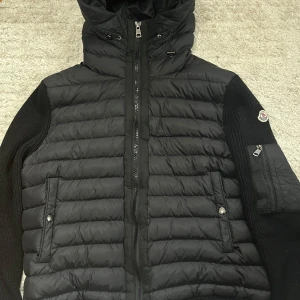  Moncler Jacka  - Snygg mörkblå pufferjacka från Moncler med stickade ärmar och detaljer. Jackan har huva, dragkedja framtill och en praktisk ficka med dragkedja på ena ärmen. Perfekt för kyliga dagar och riktigt stilren look. Storlek M men passar även xs-s. Priset kan diskuteras 