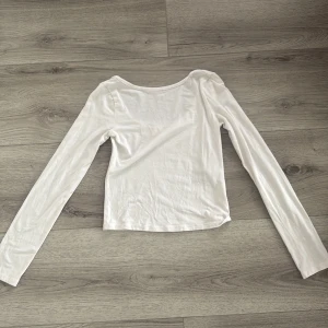 Vit långärmad topp från Gina Tricot - Enkel och stilren vit långärmad topp från Gina Tricot. Modellen har rund halsringning och är tillverkad i mjuk bomull, perfekt att matcha med jeans eller kjol för en clean look. öppen i ryggen & aldrig använd💕