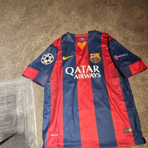Barcelona Neymar Jr 11 matchtröja - Säljer en officiell FC Barcelona matchtröja från Nike med Neymar Jr och nummer 11 på ryggen. Tröjan har breda marinblå och vinröda ränder, gula detaljer och Champions League-patch på ärmen. Materialet är lätt polyester med Dri-Fit-teknologi för extra komfort.