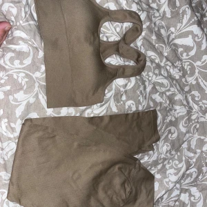 Träningsset Beige - Säljer ett beige ribbad träningsset med bred resår och brottarrygg. Toppen är ärmlös och har en tight passform, perfekt för gymmet eller yoga.  Matchandes byxor till. Snygg och enkel design som är lätt att matcha med andra träningskläder.