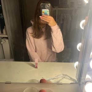 Ljusrosa hoodie med huva - Enkel och snygg ljusrosa hoodie med huva och känguruficka framtill. Tröjan har en relaxed passform och är perfekt för chill dagar. Mjuk bomullskänsla och långa ärmar gör den superbekväm att bära.