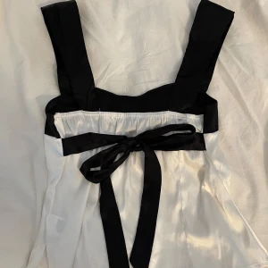 Svartvit topp med rosett på baksidan - Supersnygg linnetopp med svarta axelband och svart överdel. Toppen är vit nedtill och har en dekorativ svart rosett baktill. 