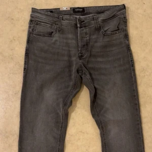 Grå slim jeans från Jack & Jones - Säljer ett par grå slim fit jeans från Jack & Jones, modell Glenn. Jeansen har klassisk femficksdesign, svarta detaljer och snygg tvättad look. Perfekta för dig som gillar en smalare passform och stilren vibe. Pris kan diskuteras 