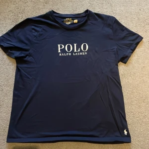 Mörkblå t-shirt från Polo Ralph Lauren - Snygg mörkblå t-shirt från Polo Ralph Lauren med klassisk logga tryckt på bröstet och liten broderad häst nertill. T-shirten har rund hals och korta ärmar, perfekt till jeans eller shorts. Materialet känns mjukt och skönt mot huden.