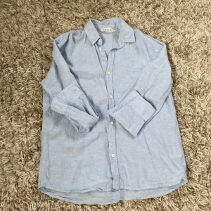 Ljusblå linne skjorta från H&M  - Snygg ljusblå skjorta från H&M i storlek 152. Skjortan är tillverkad i svalt linne, har klassisk krage, långa ärmar och knäppning framtill. Perfekt för en chill och stilren look.