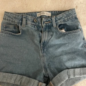 Blå mom shorts från Denim Co. - Snygga blå mom shorts från Denim Co. i klassisk jeansmodell med hög midja, uppvikta benslut och fem fickor. Tillverkade i slitstarkt bomullsmaterial och har knapp och dragkedja framtill. Perfekta för en chill och trendig look.